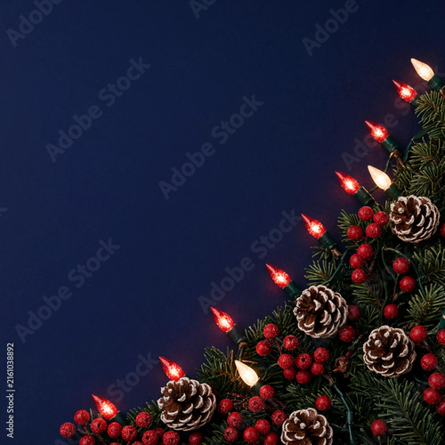 Christmas festive background with pine cones, red berries and glowing lights on dark blue