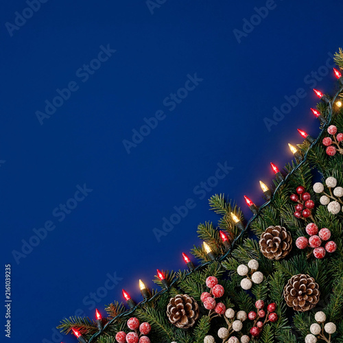 Christmas evergreen garland with red and warm lights, pinecones, and berries on blue background