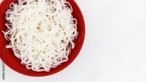 A macro, top-down close-up photograph of a bright red bowl filled completely with tangled, translucent white shirataki noodles.