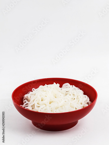 A vertical, eye-level photograph of a round red bowl centered at the bottom, filled with cooked white shirataki noodles (konjac noodles).