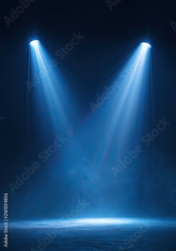 Two bright blue spotlights illuminate a smoky, dark stage