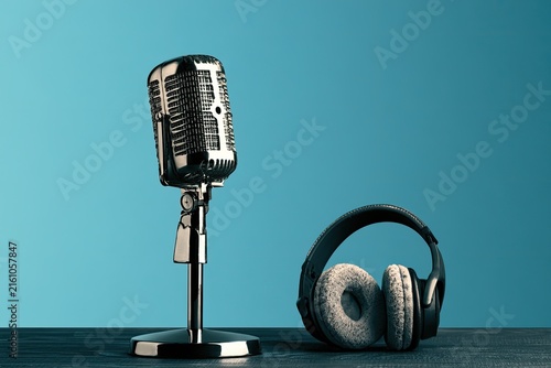 Vintage microphone and headphones rest on a wooden surface against a blue background