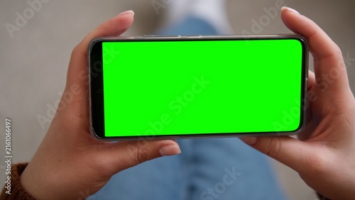 Obraz na plátně Top view of woman hands holding smartphone horizontally with green screen mockup chroma key blank display