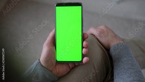 Obraz na plátně Top view of man holding smartphone vertically with green screen mockup chroma key blank display