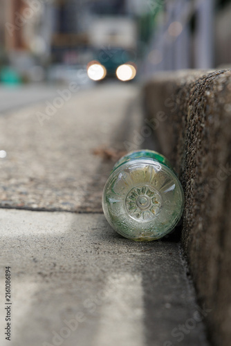 Condensation‑covered plastic bottle lying as litter beside a city street curb, with blurred car headlights in the background.