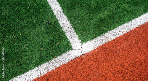 Top down view of artificial green grass turf and red running track separated by white line marking