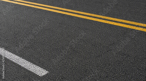 Close up view of dark asphalt road texture with yellow double lines and white line marking