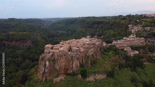 Aerial view of the historic hilltop village of Calcata Vecchia with stone houses perched on a cliff above a lush green valley in Calcata Vecchia, Lazio, Italy.