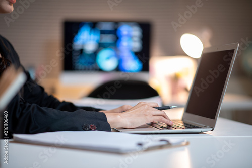 Businesswoman Working on Laptop at Office Desk with Data Dashboard on Monitor in Background