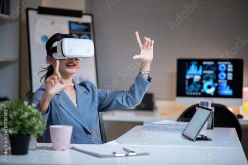 Asian Businesswoman Using VR Headset in Modern Office with Digital Dashboard Displays
