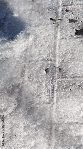 Frozen paving stones covered in a melting layer of ice. A close-up of a pedestrian path in winter and spring.