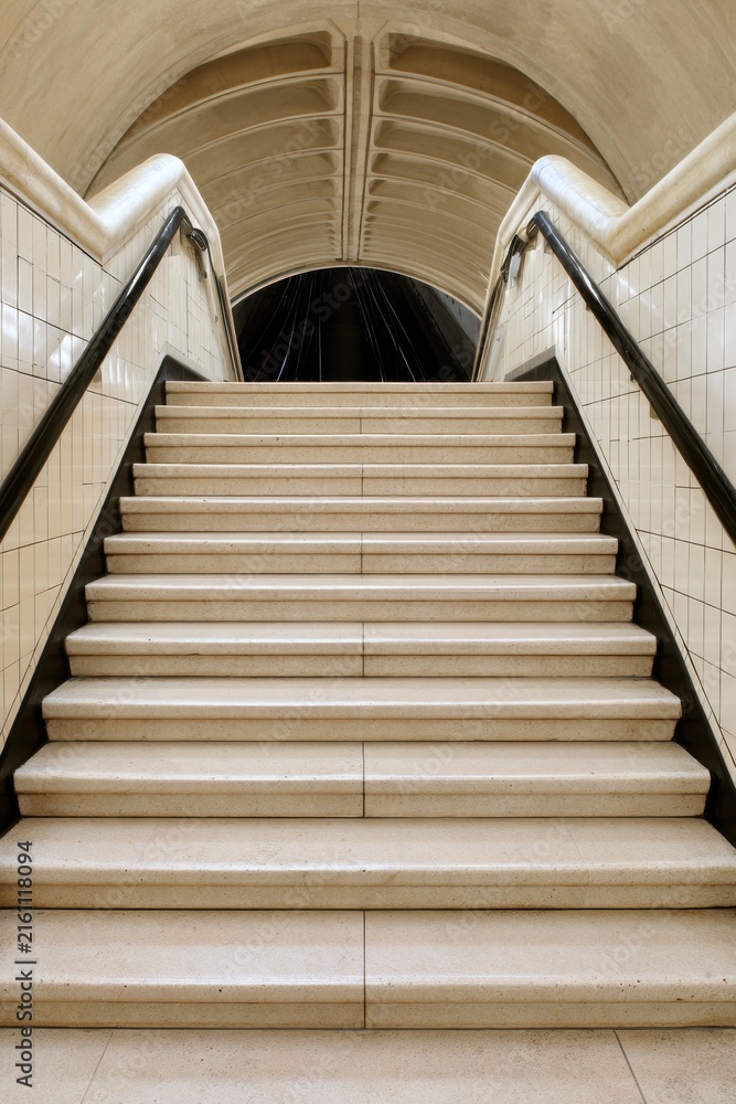 Obraz premium Stone staircase descending to underground platform with arched ceiling and handrails for interior background and architectural design
