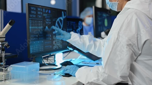 Focused scientist in hazmat suit analyzes brain scan data on high-tech monitors and writes clinical research notes in modern medical laboratory.