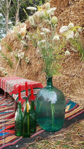 Fotografía Vintage green glass carboy with wild white flowers and wax dripping bottles on t