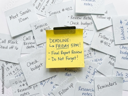 Deadline reminder written on a yellow sticky note surrounded by cluttered notes and paperwork