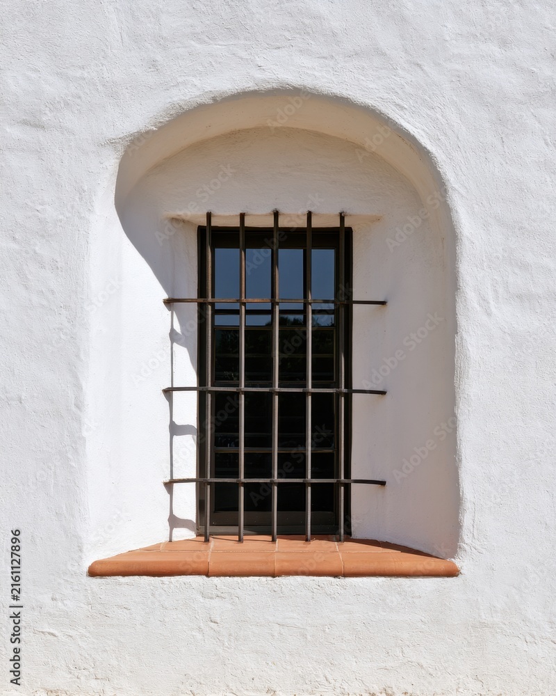 Obraz premium Mediterranean arched stucco window with iron bars and terracotta sill for architectural background, facade design, travel imagery and minimal interior decor