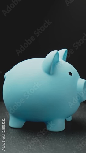 Piggy bank as concept for storing, accumulating, and saving financial resources. Vertical video. Charming blue piggy bank rotating on dark background. Close-up in 4K, UHD