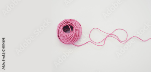 Una matassa di spago di colore rosa in primo piano su una superficie bianca e vuota con spazio per testo
