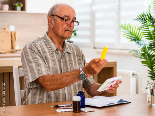 Senior man taking medicine from a pill organizer at home, following his daily health care routine and carefully preparing the right dose.
