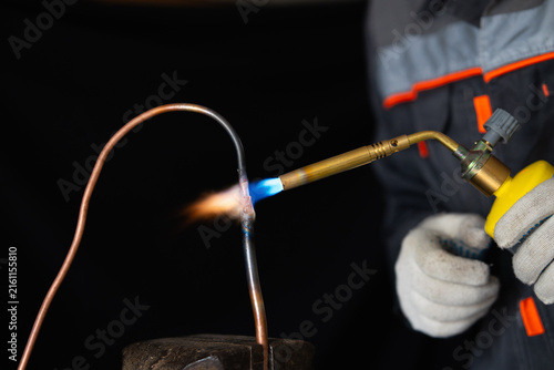 Foto Close-up of a worker in protective gloves brazing a copper pipe with a gas torch