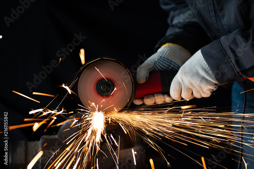 A worker uses an angle grinder to cut metal clamped in a heavy bench vice