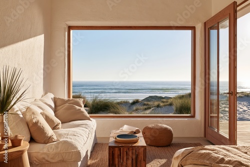 sunlit coastal living room with panoramic ocean view, natural linen sofa, rustic wooden furniture and open doors overlooking sandy dunes and the sea