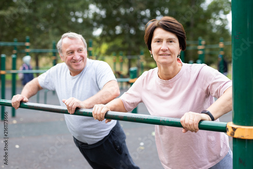 Elderly couple doing push-ups on crossbar together on sports ground of city park