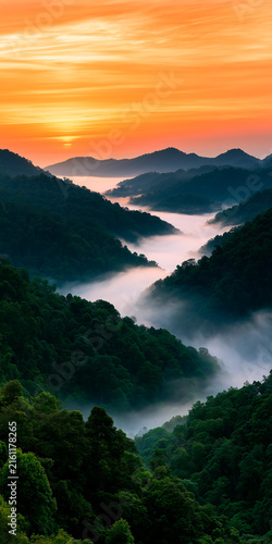 Misty mountains at sunrise with lush tropical forest. Orange sky above green jungle peaks. Morning fog rolls through valleys creating scenic landscape