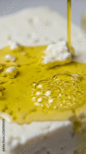 Golden olive oil pouring over white cheese block