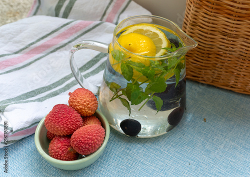 Фотография Clear infused water with whole and sliced lemon Citrus limon and fresh mint Mentha leaves served in a glass pitcher beside ripe lychee fruit Litchi chinensis