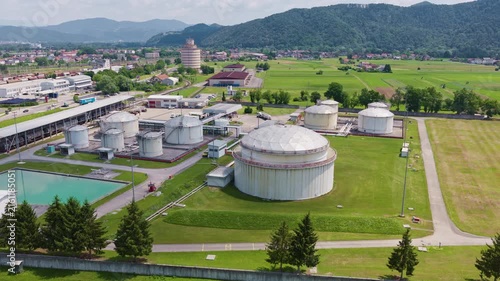 Large industrial oil storage tanks are seen at a petroleum depot with green fields nearby. The view shows energy infrastructure in the area.