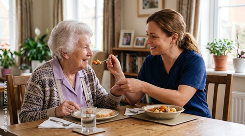 Caring Companion: A compassionate caregiver lovingly feeds a senior woman, sharing a warm moment of connection over a meal at a dining table, highlighting the essence of tender care.