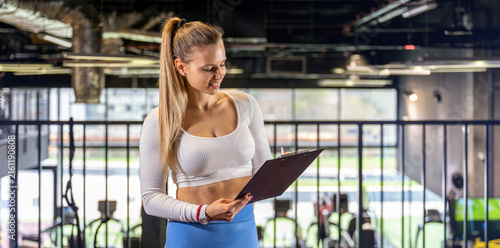 Female personal fitness coach examining training schedule on clipboard indoors.
