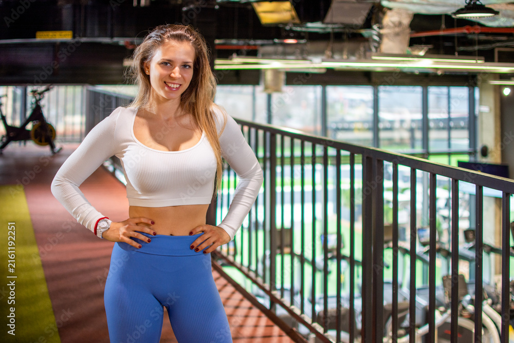 Fototapeta premium Smiling fit woman standing near balcony railing posing confidently in modern gym.