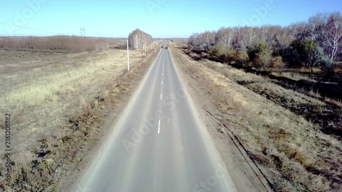 Aerial view of a long straight empty asphalt road passing through autumn fields and birch forests under a clear blue sky. Empty highway road trip concept.