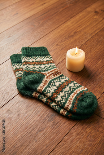 Cozy knitted socks beside a candle on a wooden surface  