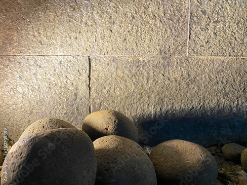 Canvas Print Smooth river stones illuminated by warm spotlight against a textured stone wall