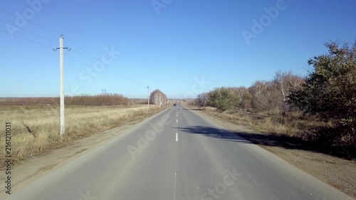 Straight empty asphalt road stretching into the horizon through rural countryside under clear blue sky in autumn
