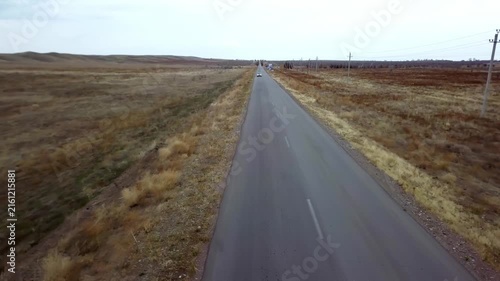 Aerial view of a long straight asphalt road passing through dry open steppe landscape on an overcast day
