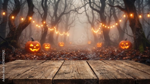 Empty wooden table with Halloween background of glowing pumpkins and string lights in foggy autumn forest at night