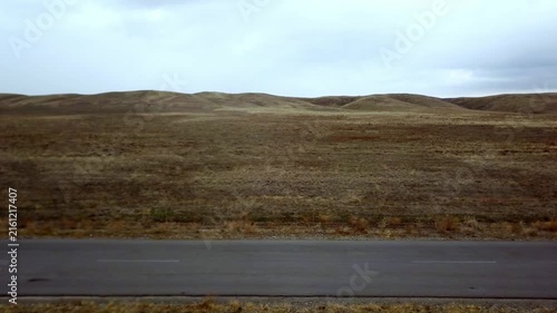 Empty asphalt road through dry steppe and hills under overcast sky