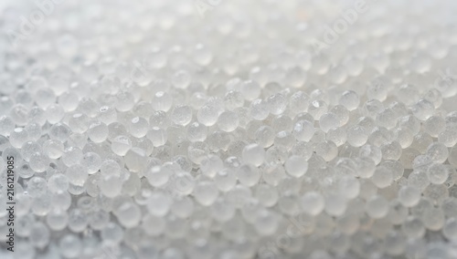 White plastic polymer pellets pouring from an industrial machine into a large storage container in a manufacturing facility.