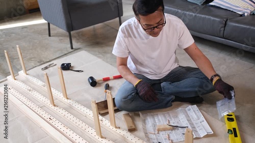 Furniture assembly man using instruction guide and tool for wood home project building flat pack shelf on floor