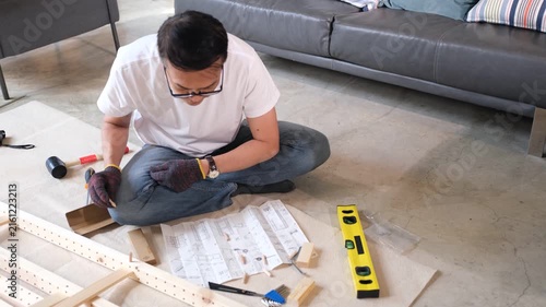 Furniture assembly man uses tool and instruction level in living room building wood frame on floor for home project