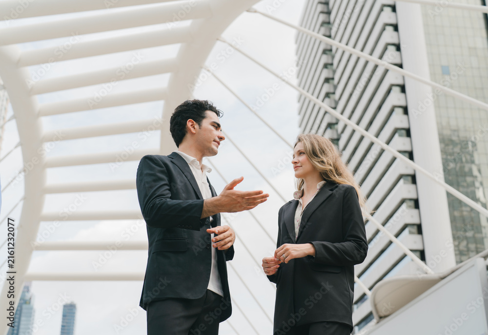 Fototapeta premium Businessman explaining with hand gesture to businesswoman on a modern skybridge with city skyscrapers, business discussion, presentation and corporate collaboration.