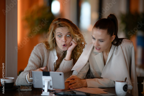 Fotografie Two businesswoman colleagues react in disbelief to something on a tablet during