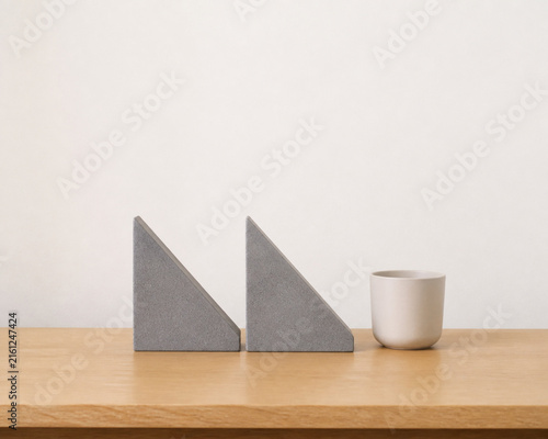 Two identical triangular bookends in row on oak desk with ceramic cup, minimalist desk organization concept