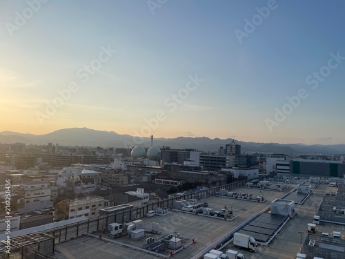 Tapety artystyczne 夕暮れの京都の街並み、屋上駐車場と山々