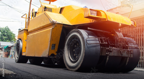 Canvastavla Yellow road roller compactor working on freshly paved asphalt, showing heavy construction machinery used for roadwork, pavement repair, street maintenance and infrastructure development