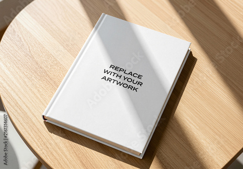 Hardcover book mockup with replace your artwork text displayed on a wooden table in an interior setting natural light, product presentation, graphic design template